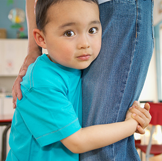 Preschool boy holding on to his moms leg.