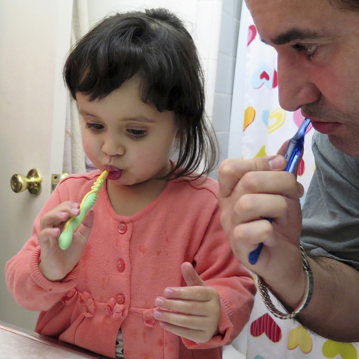 Hombre y niña pequeña cepillándose los dientes en el baño.